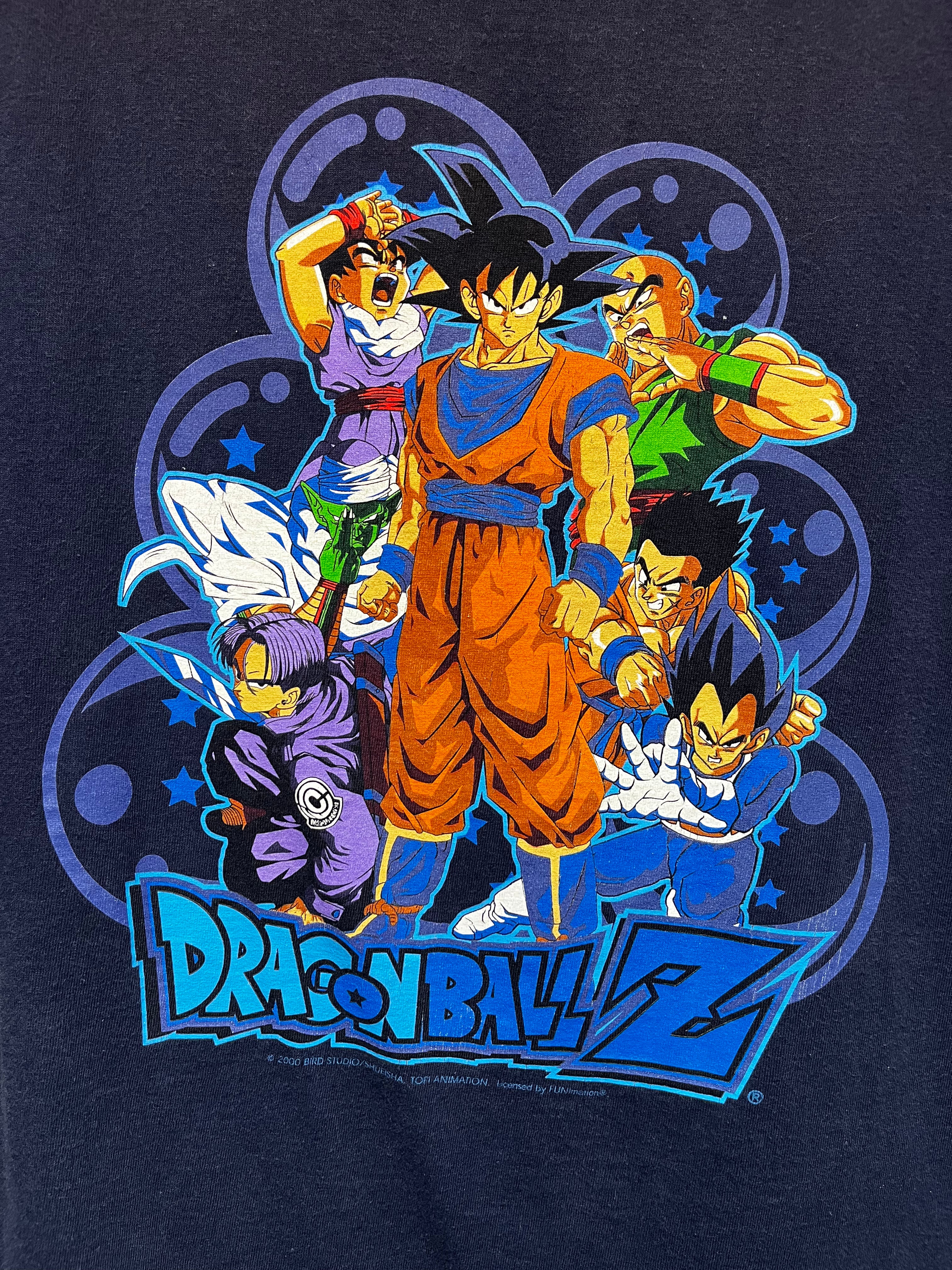 A close-up of a dark navy blue graphic t-shirt featuring the Dragon Ball Z characters Goku, Vegeta, Gohan, Krillin, and Barda in a dynamic group pose above the 'Dragon Ball Z' logo.